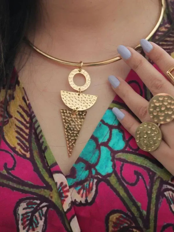 Gold necklace with geometric pendant worn by a person against a colorful background